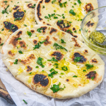 3 garlic naan on a parchment paper with garlic ghee bowl on the side.