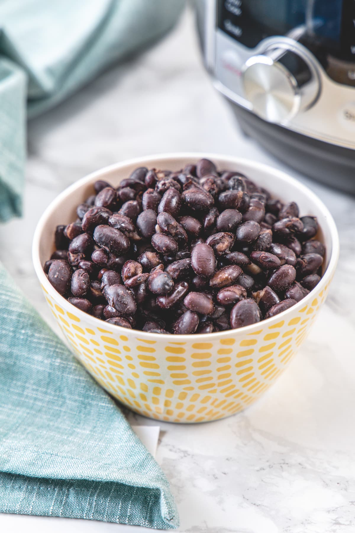 Cooked black beans in a bowl with napkin on the side and instant pot in the back.