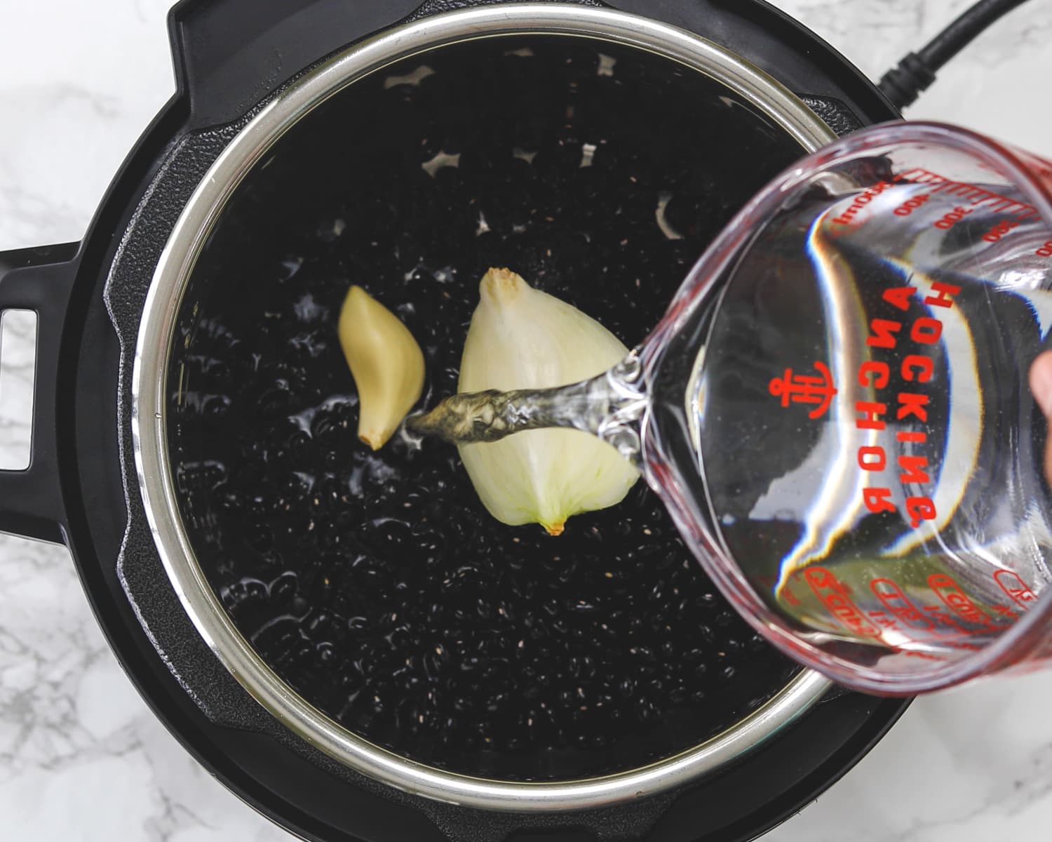 Adding water in instant pot with dry beans, onion, garlic and salt.