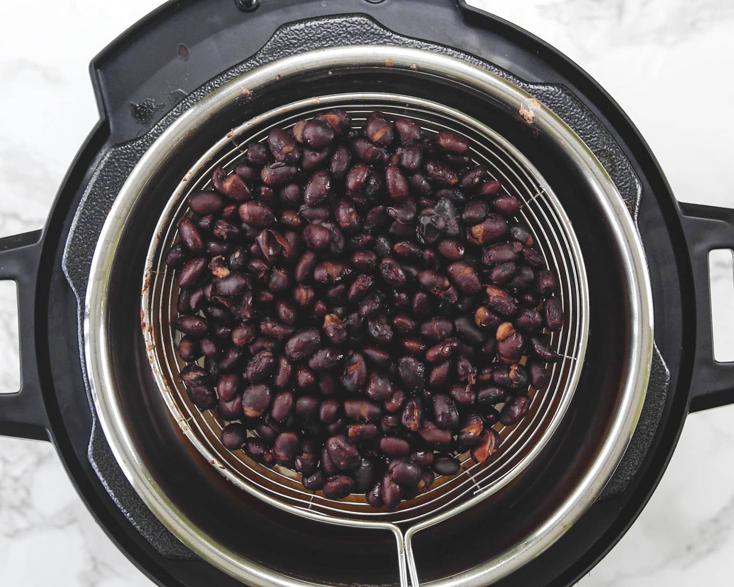 Cooked black beans in a strainer rested on instant pot liner.