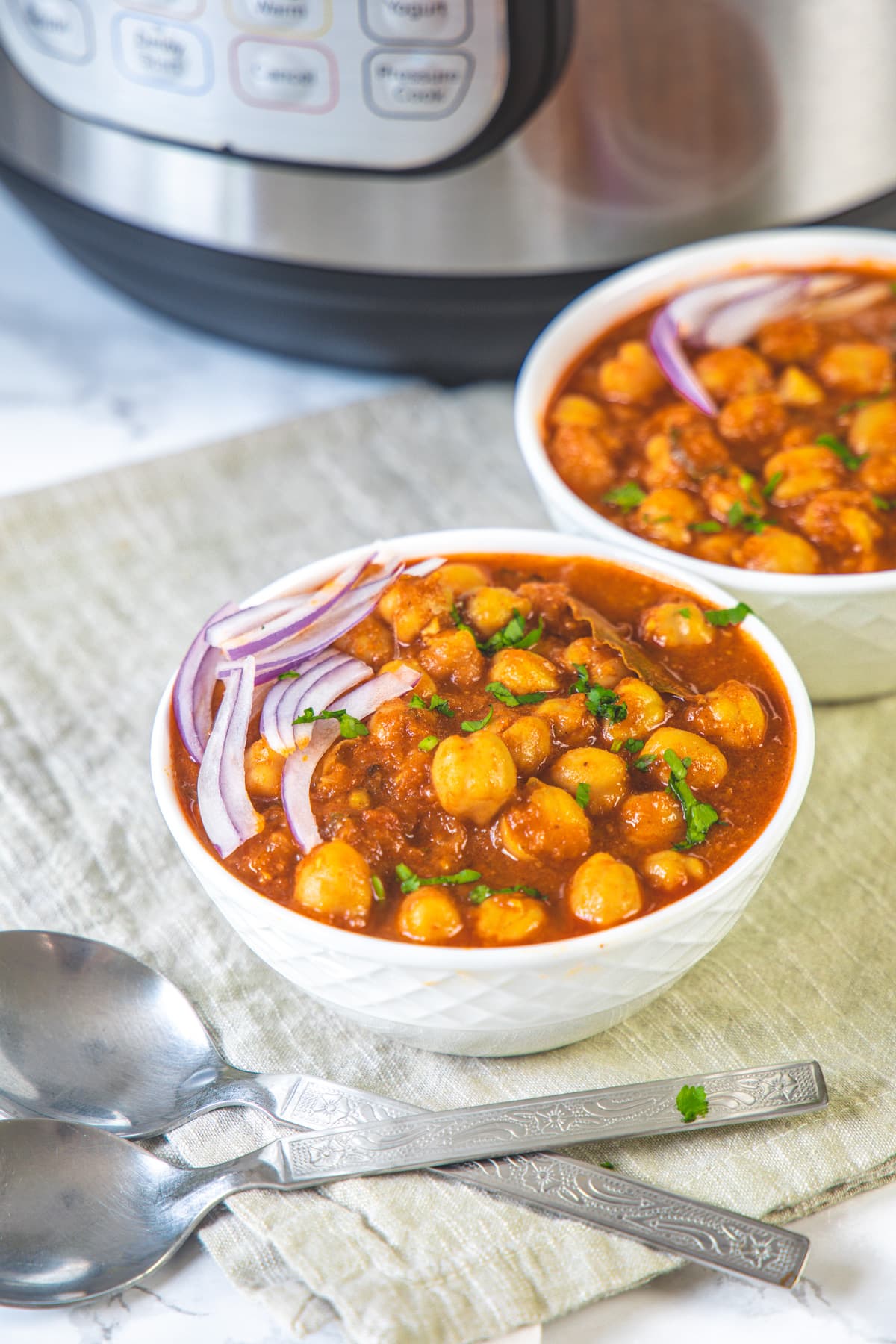 2 bowl of chana masala with sliced onions and spoons on the side.