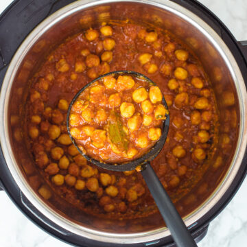 A ladleful of chana masala is taking from instant pot.