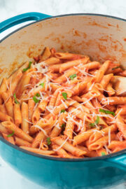 Pink sauce pasta in dutch oven garnished with parmesan cheese and basil.