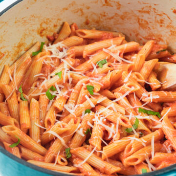 Pink sauce pasta in dutch oven garnished with parmesan cheese and basil.