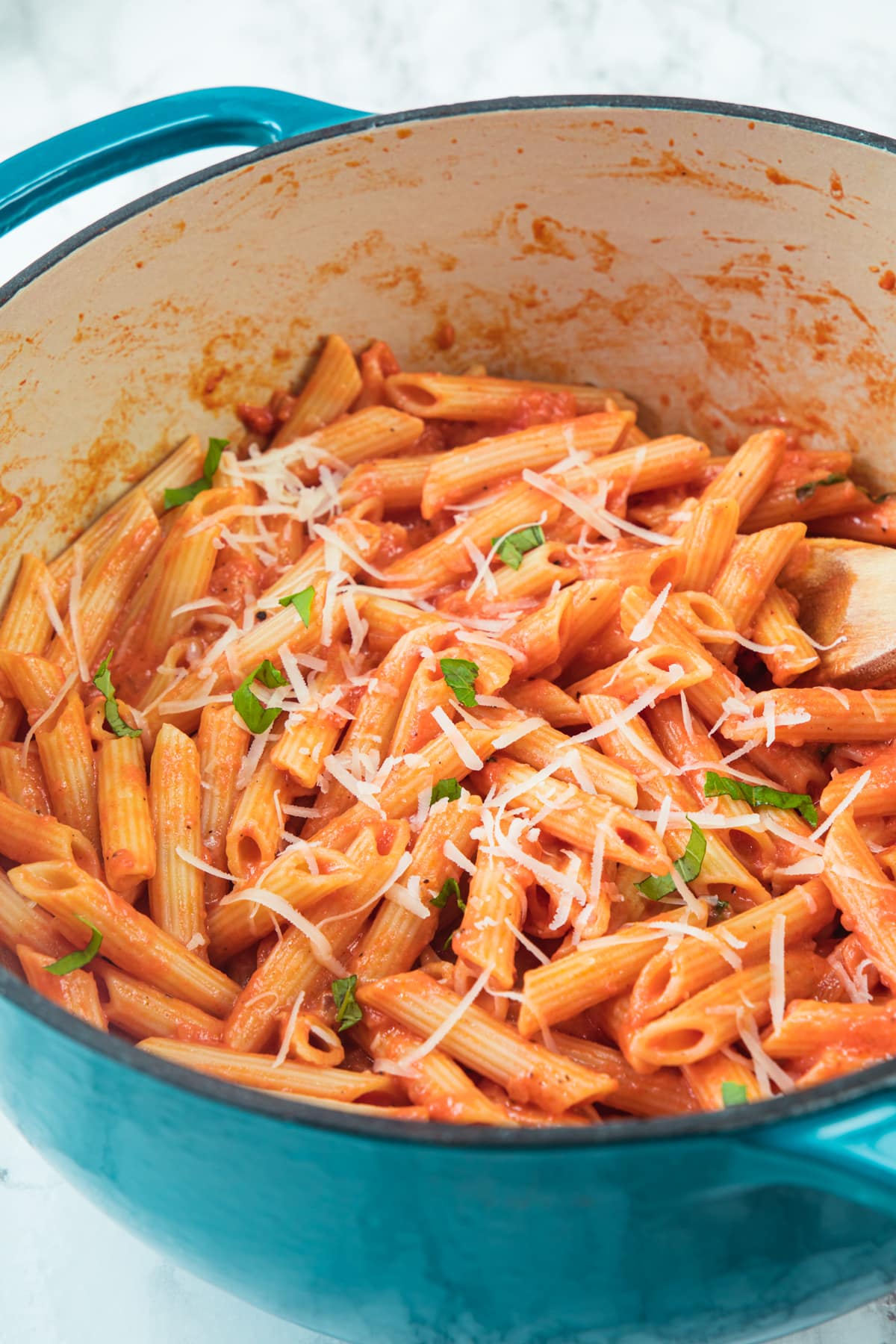 Pink sauce pasta in dutch oven garnished with parmesan cheese and basil.