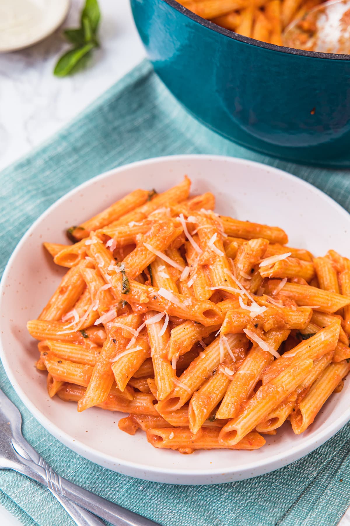 Pink sauce pasta served in a plate with napkin under it and fork on the side.