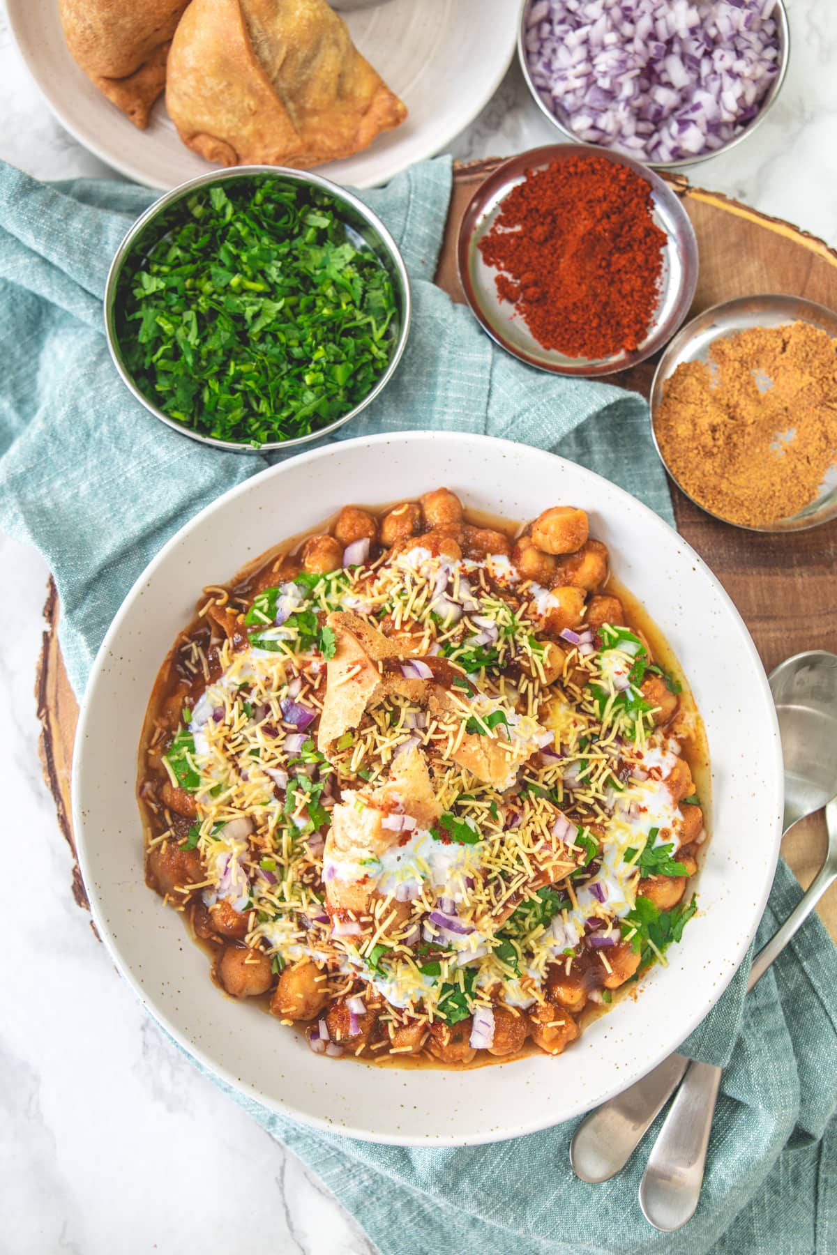 A plate of samosa chaat with a napkin under the plate with extra elements on the side.