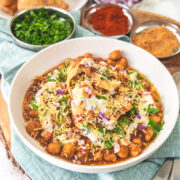 A plate of samosa chaat with more samosa, onion, chutney, cilantro in the back.