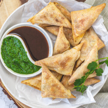 Paneer samosa in a plate with green chutney and tamarind date chutney.