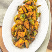 A plate of brussels sprouts curry on a wooden board with napkin under the plate.