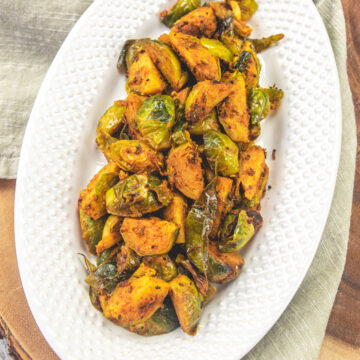 A plate of brussels sprouts curry on a wooden board with napkin under the plate.