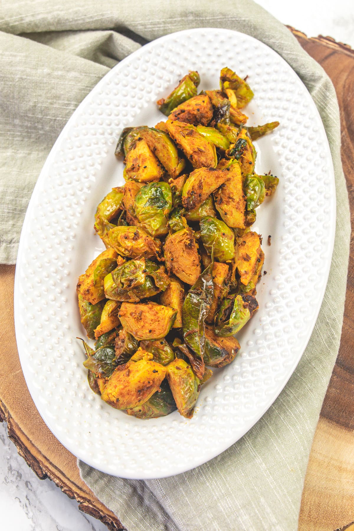 A plate of brussels sprouts curry on a wooden board with napkin under the plate.