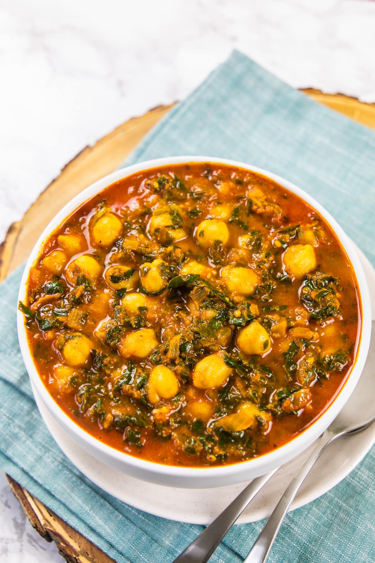 Chana saag in a bowl with spoons on the side and napkin under it.