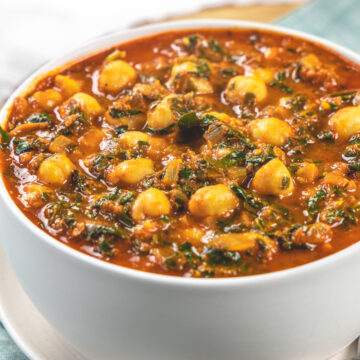 Chana saag bowl in a plate with 2 spoons in the plate.