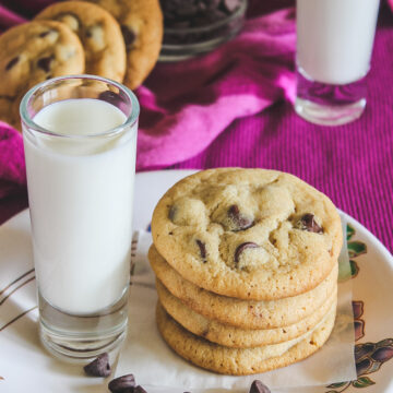 A stack of eggless chocolate chip cookies with a glass of milk.