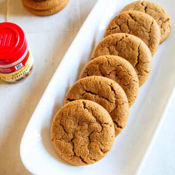 Eggless ginger cookies in a rectangle plate with a stack of cookies in the back.