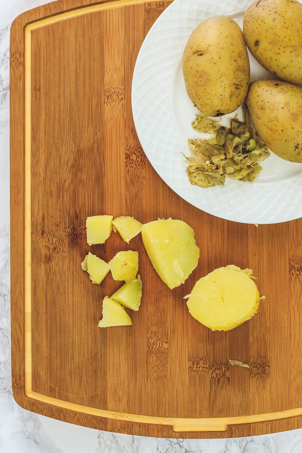 Cut potato in half and cubes on a chopping board and 3 potatoes in a plate.