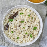 Jeera rice plate with a bowl of dal in the back.