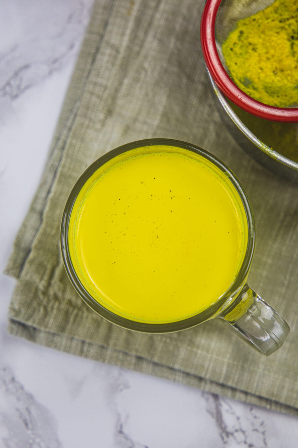 Haldi doodh in cup with strainer behind it.