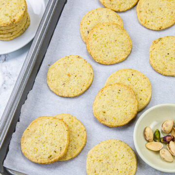 Pistachio cookies in a tray with pistachios on the side.