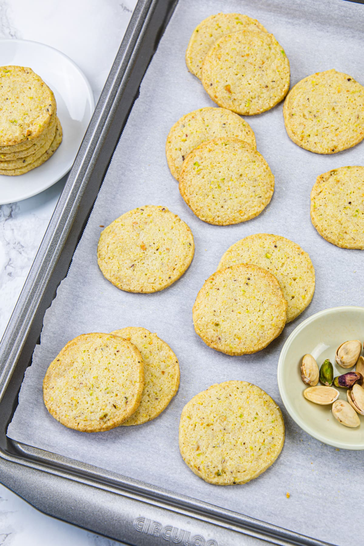 Pistachio cookies in a tray with pistachios on the side.