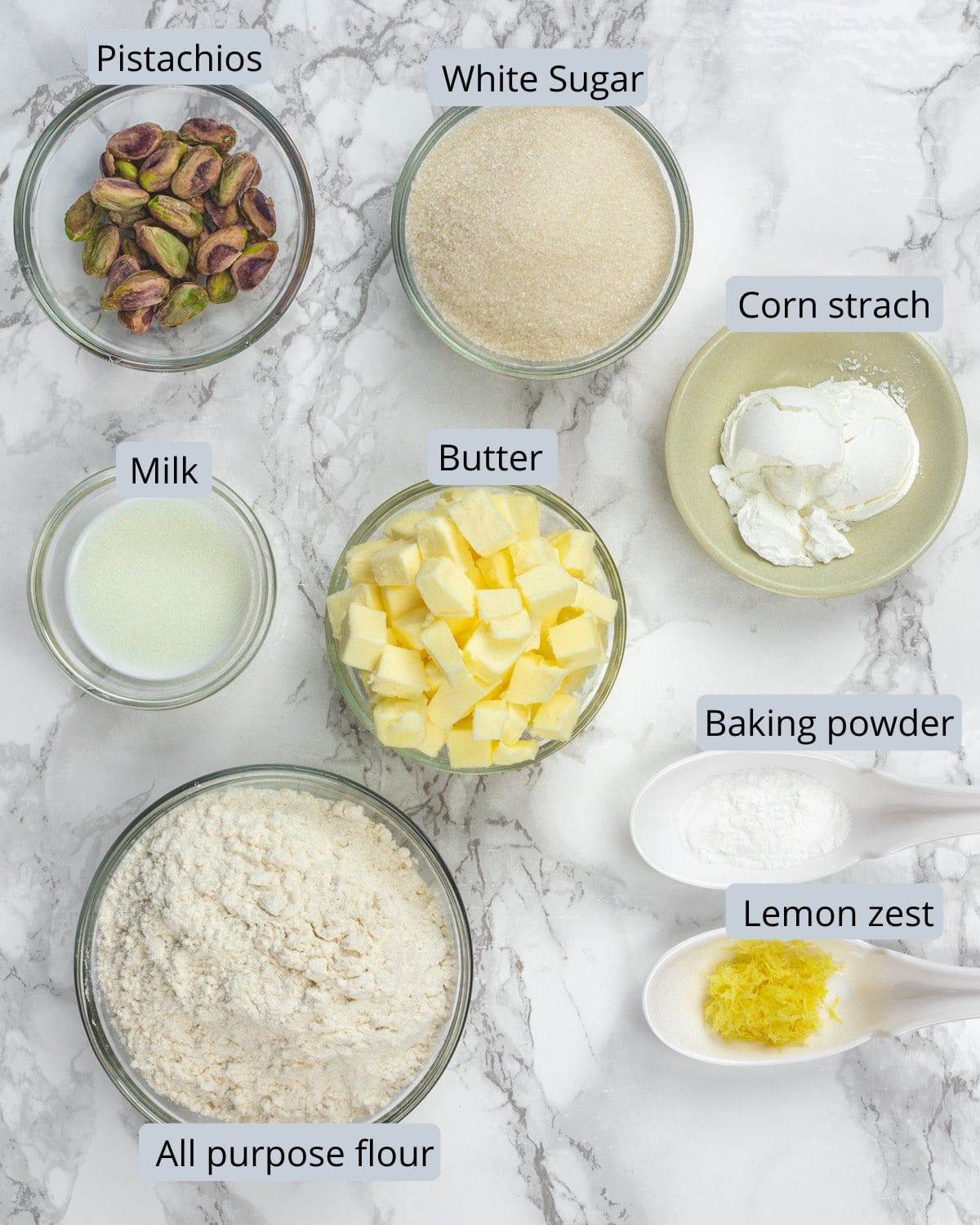 Pistachio cookie ingredients in bowls and spoons with labels.