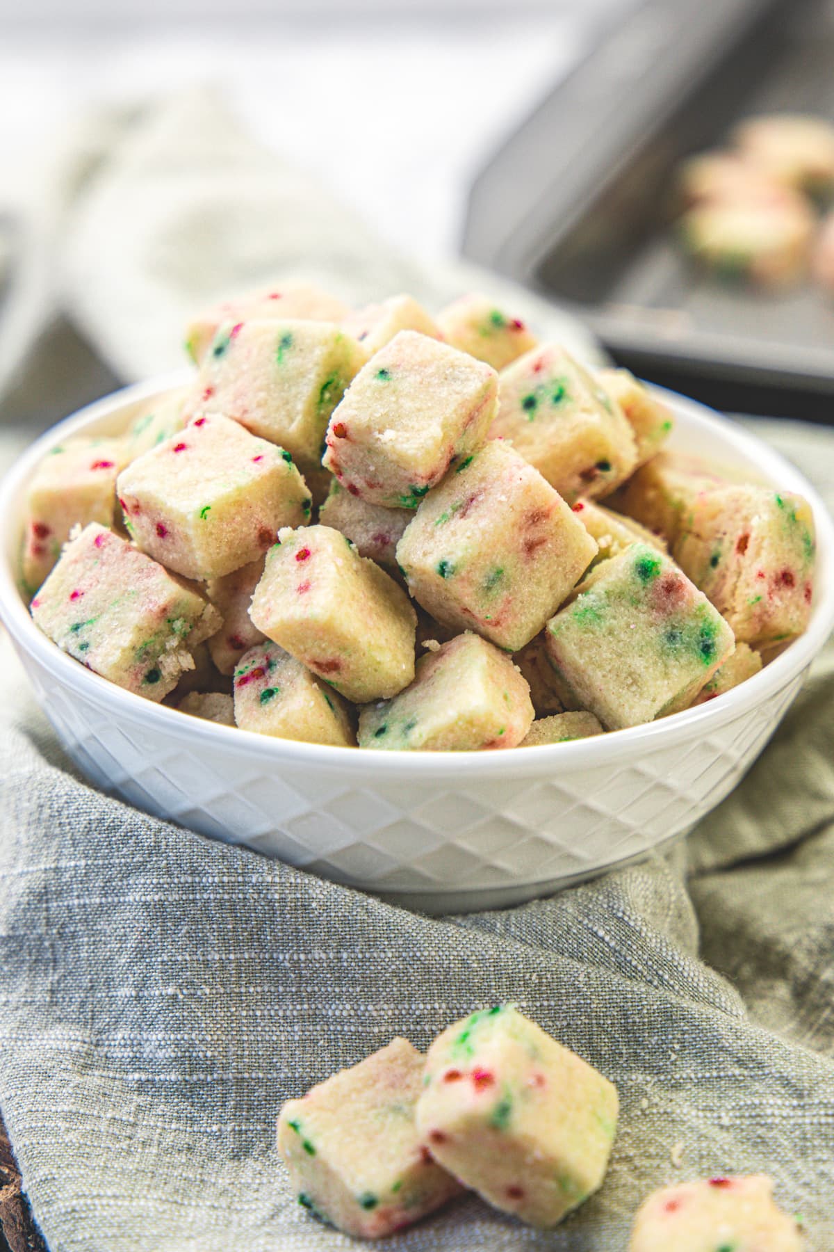 A bowlful of shortbread bites with more in the tray in the back and a few on the napkin.