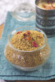 Thandai powder in a glass jar garnished with rose petals.