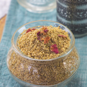 Thandai powder in a glass jar garnished with rose petals.