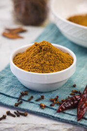 Chana masala powder in a bowl with whole spices around the bowl.