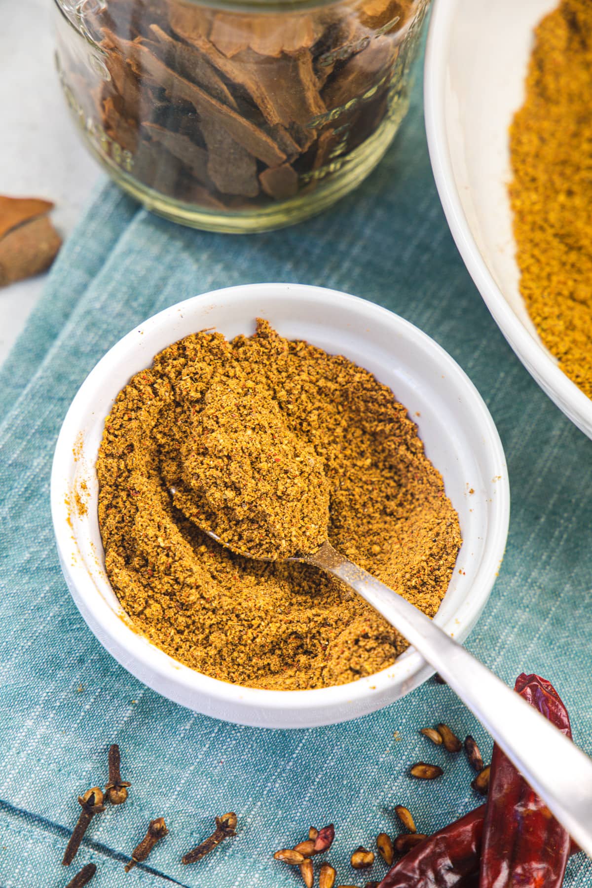 Chana masala powder in a white bowl with a spoon inside.