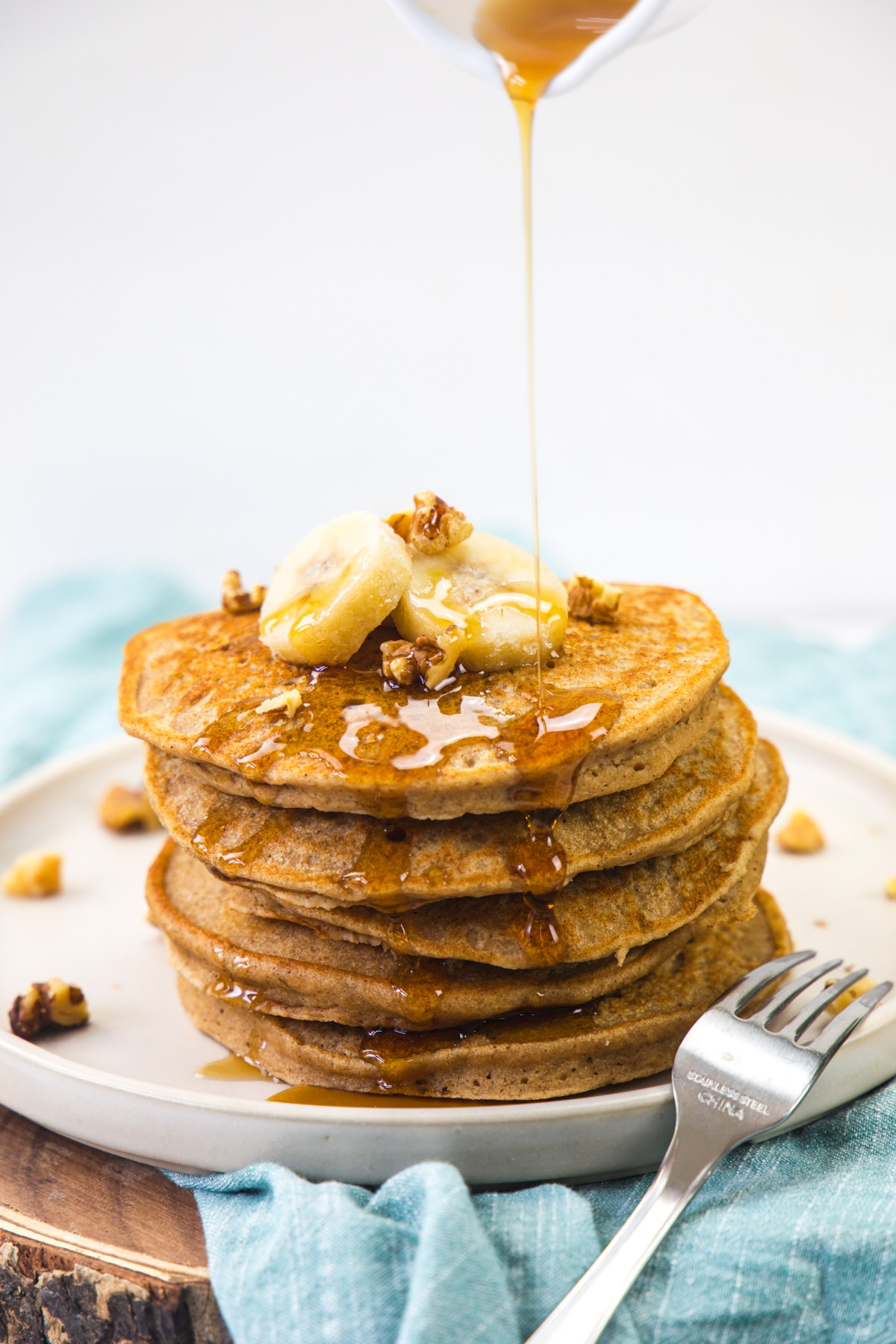 A stack of eggless banana pancakes topped with banana, nuts and drizzling syrup.