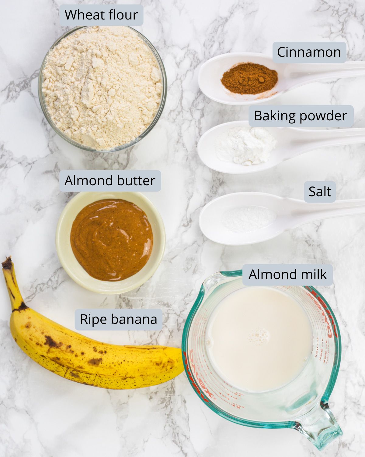 Eggless banana pancakes ingredients in bowls and spoons with labels.