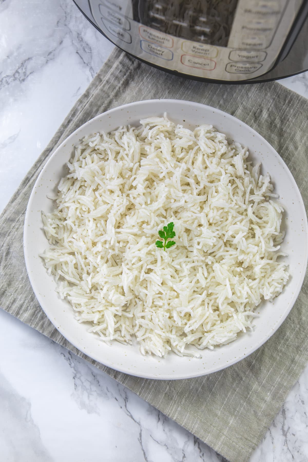 Instant pot basmati rice in a plate garnished with cilantro with napkin under and instant pot in the back.