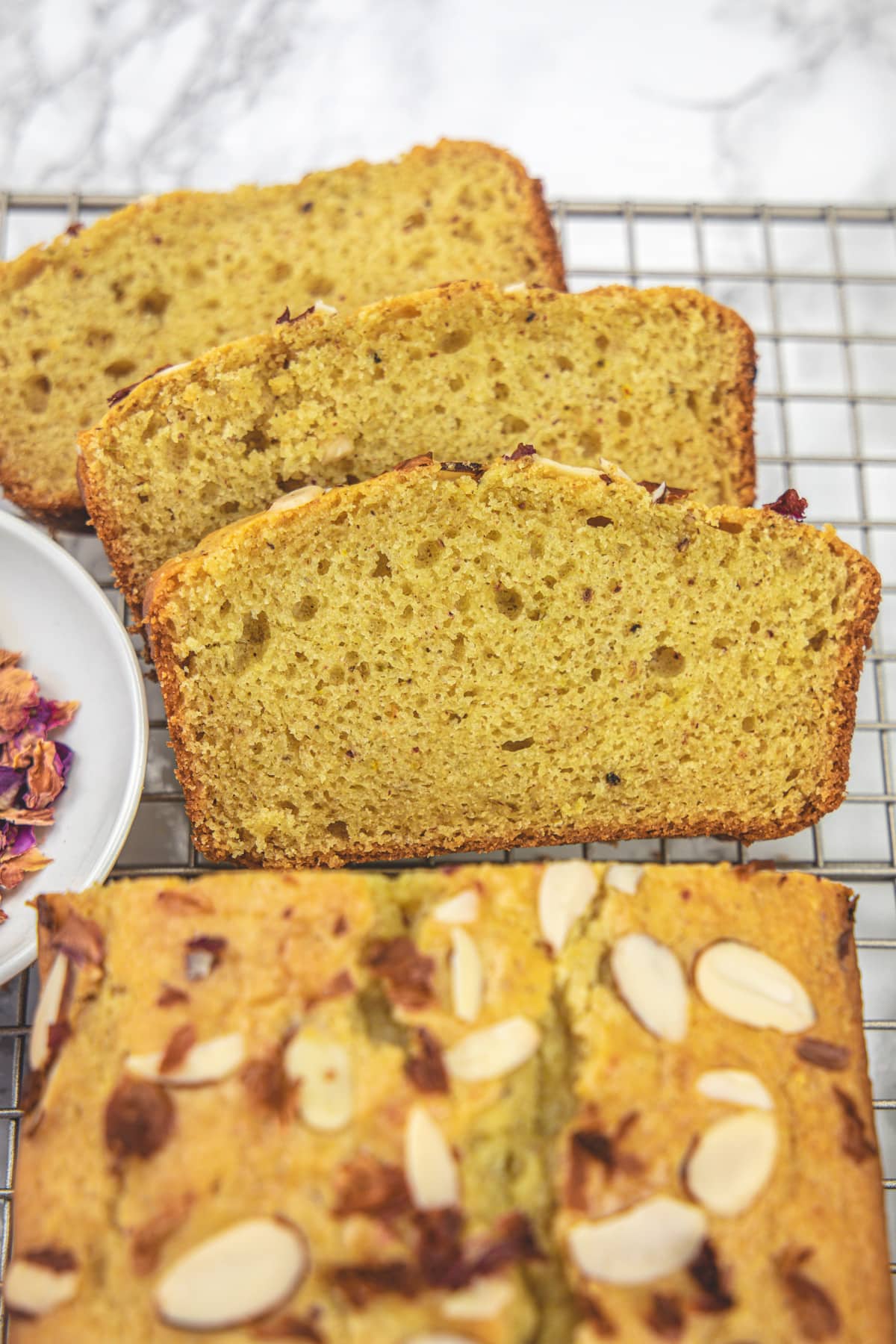 3 slices of thandai cake on a cooling rack with rest of the loaf.