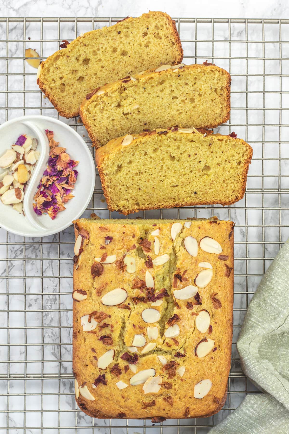 3 slices of thandai cake and rest of the loaf with rose petals and almonds on the side.