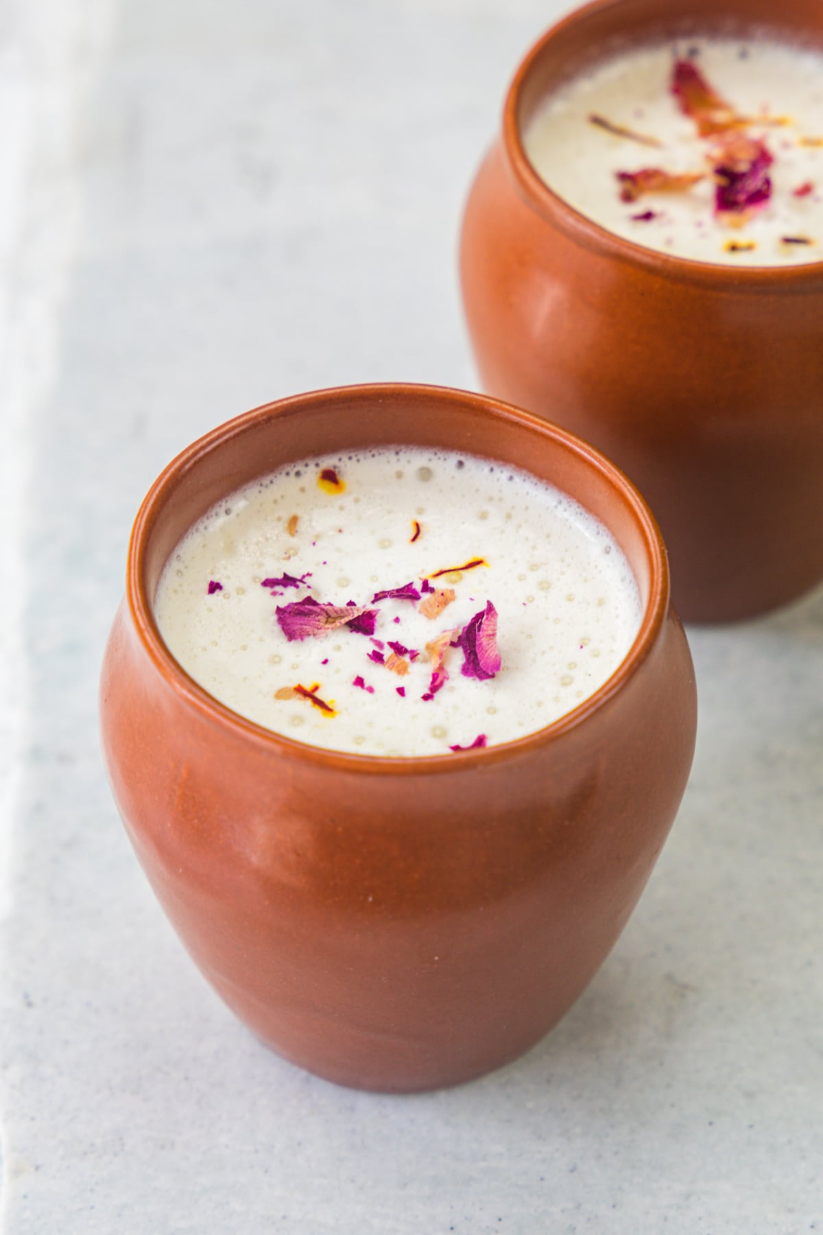 Thandai served in clay glass and garnished with rose petals and saffron.