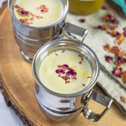 2 glasses of thandai with syrup in the back and rose petals around.