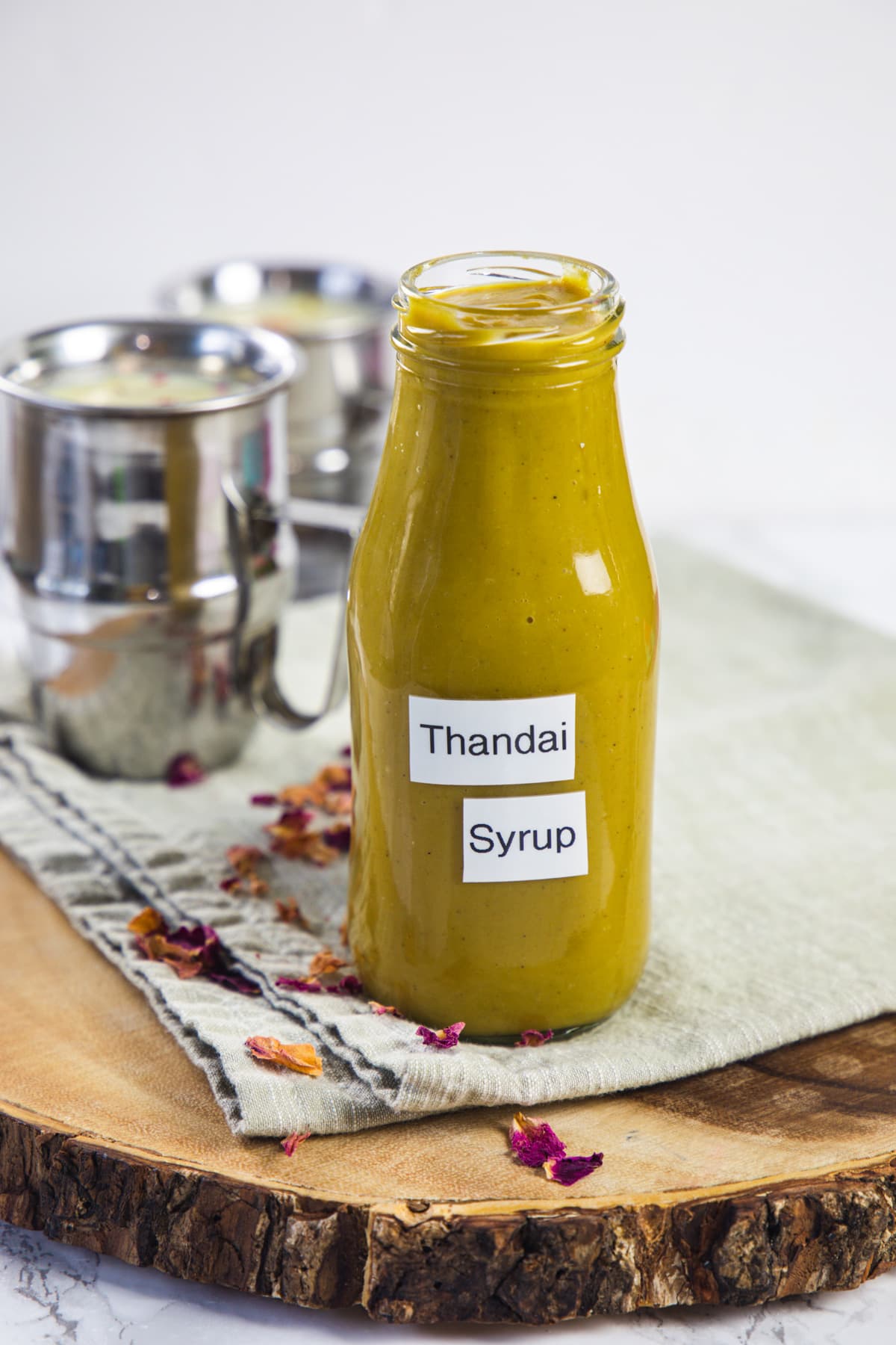 Thandai syrup with label on the jar with thandai glasses in the back.