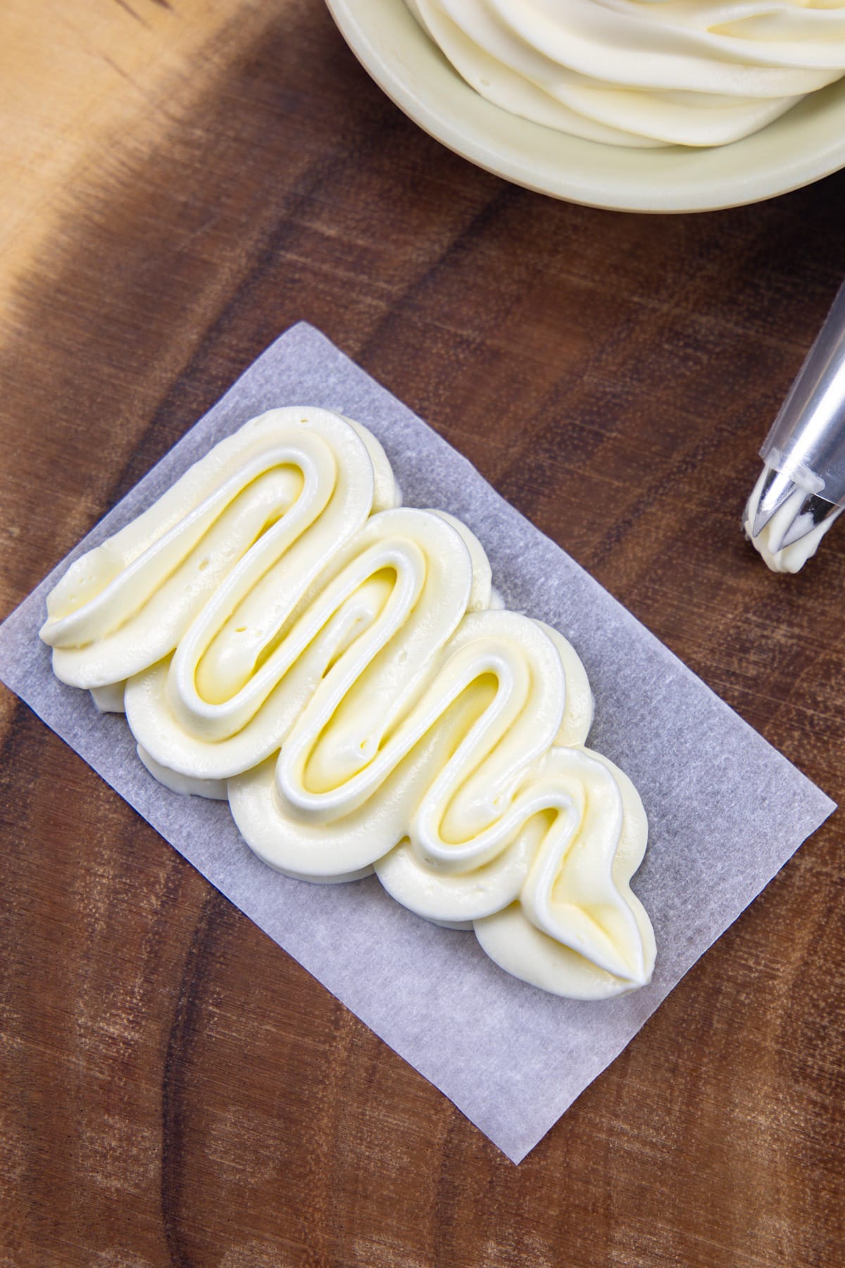 Whipped cream cheese frosting piped on a parchment paper with piping bag on th side.