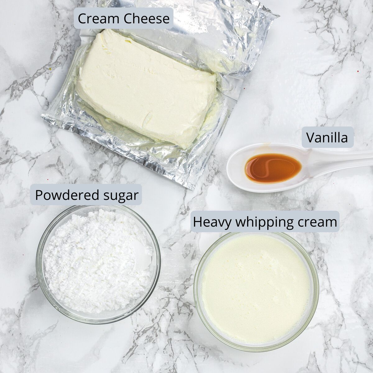 Whipped cream cheese frosting ingredients in bowls and spoon with labels.