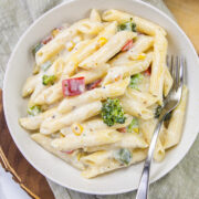 White sauce pasta in a plate with a fork and napkin under it.