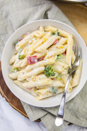 White sauce pasta in a plate with a fork and napkin under it.