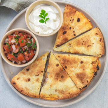 Air fryer quesadillas in a plate with a bowl of pico de gallo and sour cream.