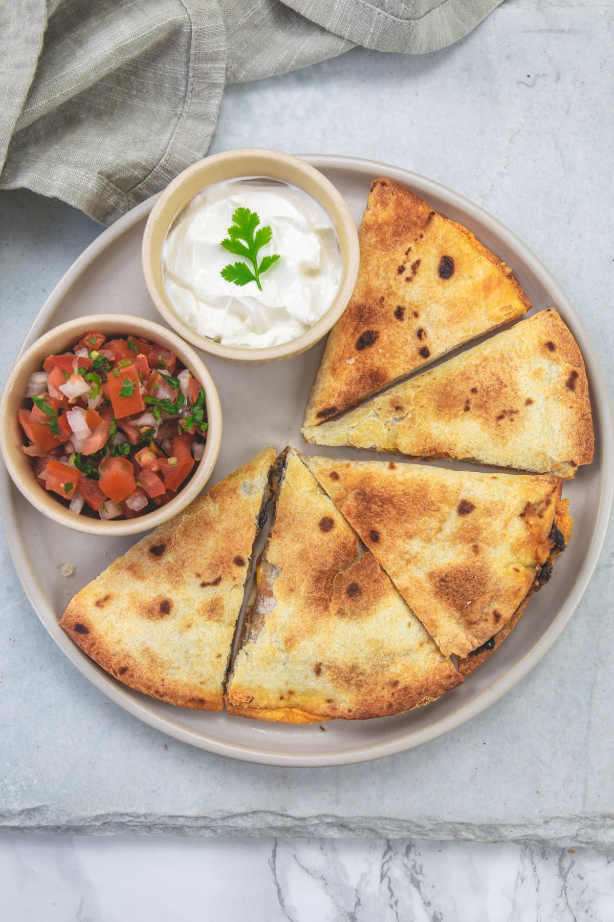 Air fryer quesadillas in a plate with a bowl of pico de gallo and sour cream.