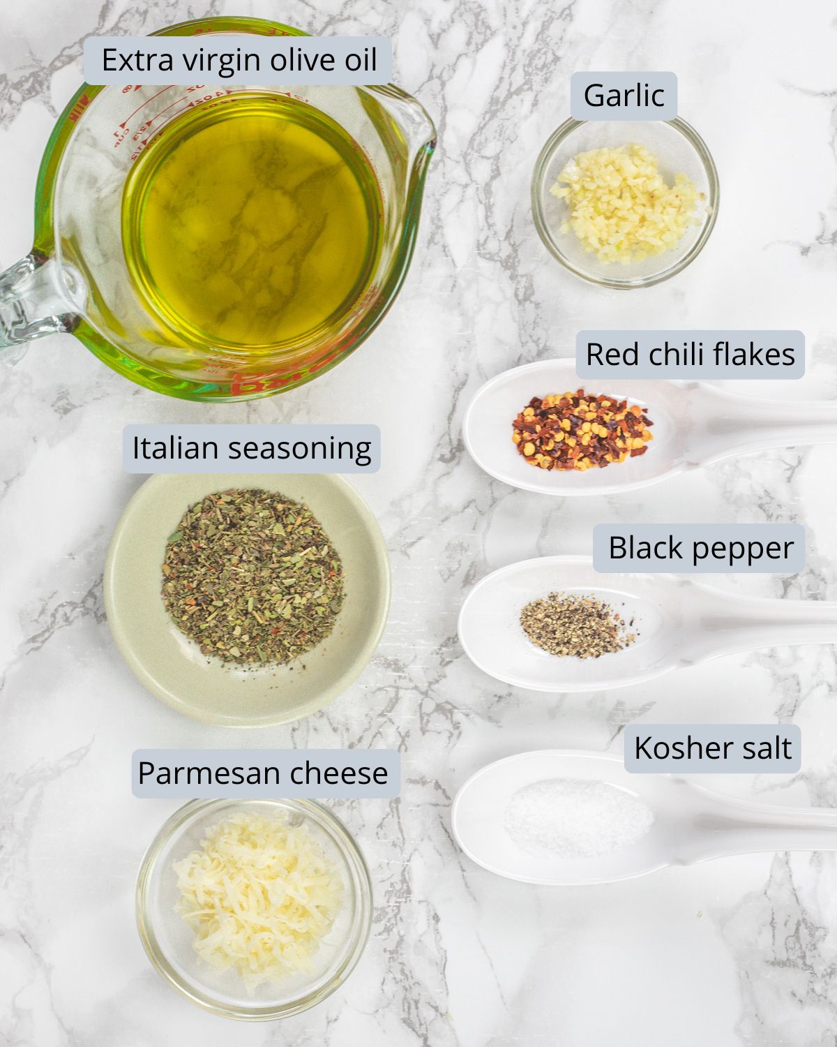 Bread dipping oil ingredients in a cup and spoons with labels.