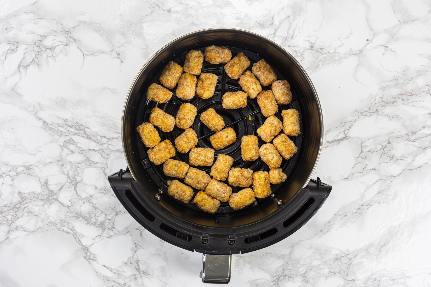 Frozen tater tots in air fryer basket.