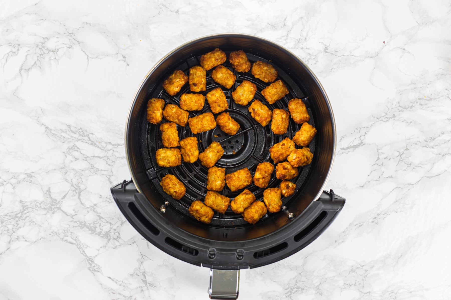 Air fryer tater tots ready in air fryer basket.