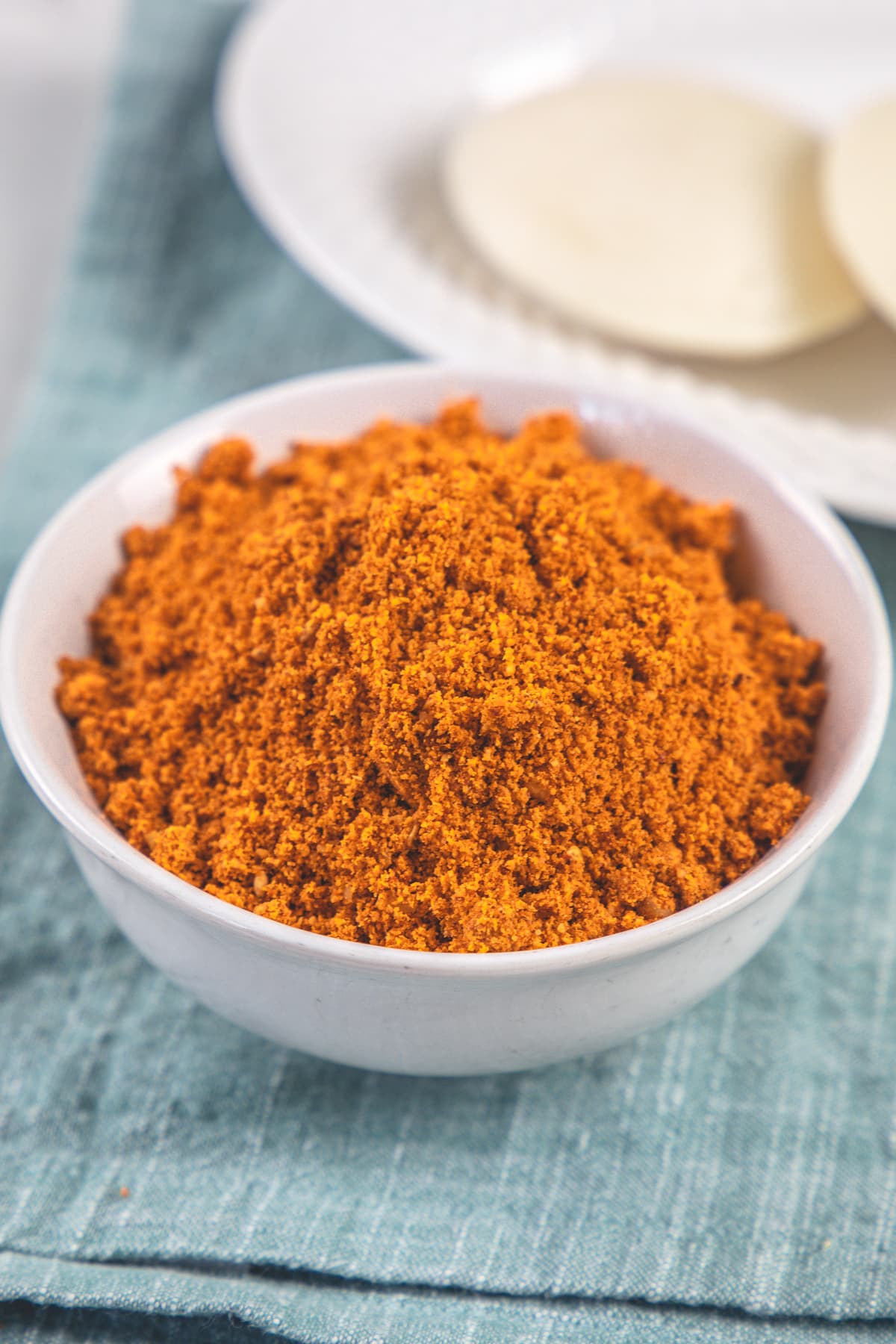 Idli milagai podi in a bowl with idlis in back.