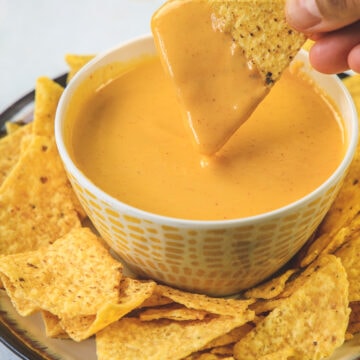 Tortilla chip dipped into nacho cheese sauce.